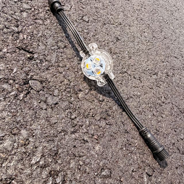 A single clear RGBW LED puck light on a short black lead with a connector at each end