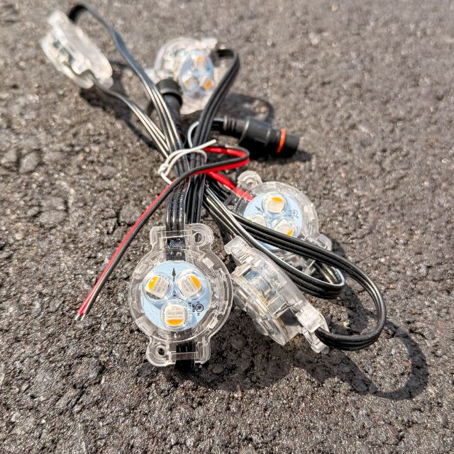 Clear RGBW puck lights on a black strand with a red and black power-injection lead joined into the run