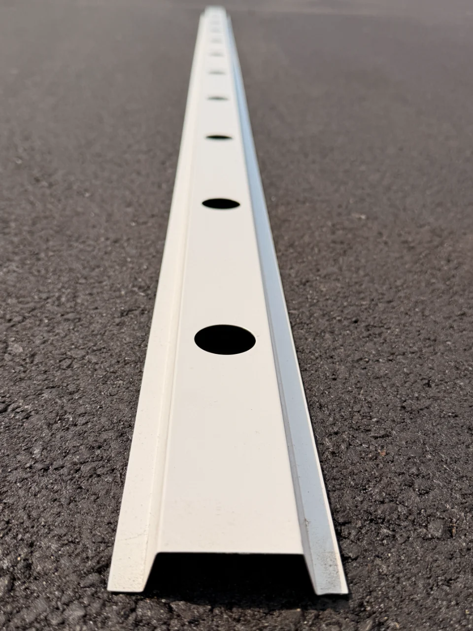 A stick of white aluminum standard hat track seen end-on down its length, pre-drilled mounting holes along the face